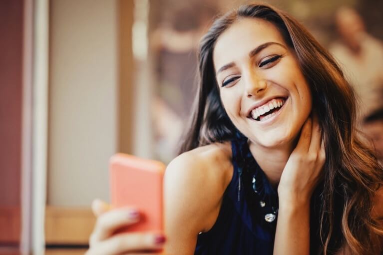 Mulher bonita a sorrir em frente ao telemóvel.
